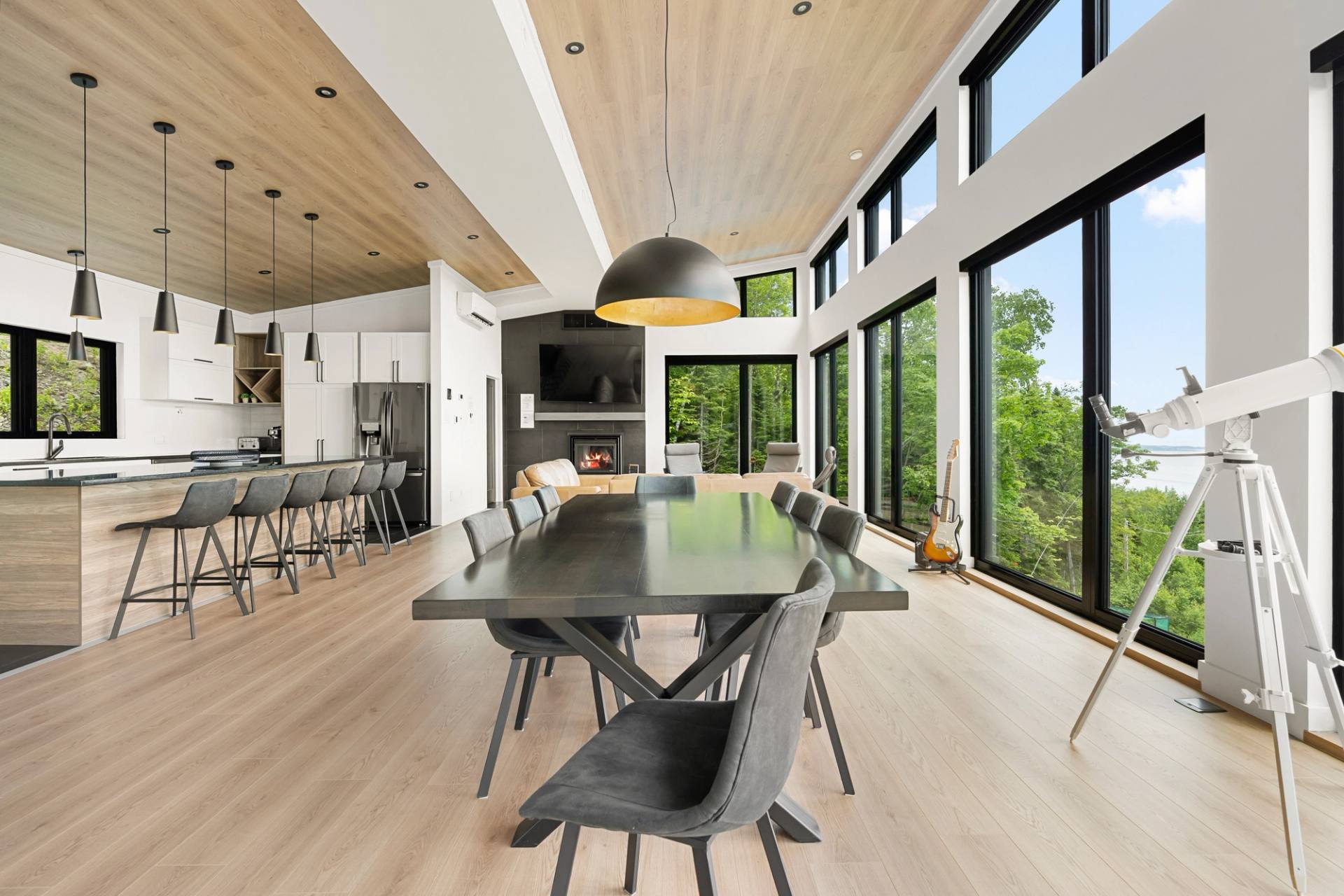 Salle a manger baignee de lumiere sous une suspension noire, grandes fenetres