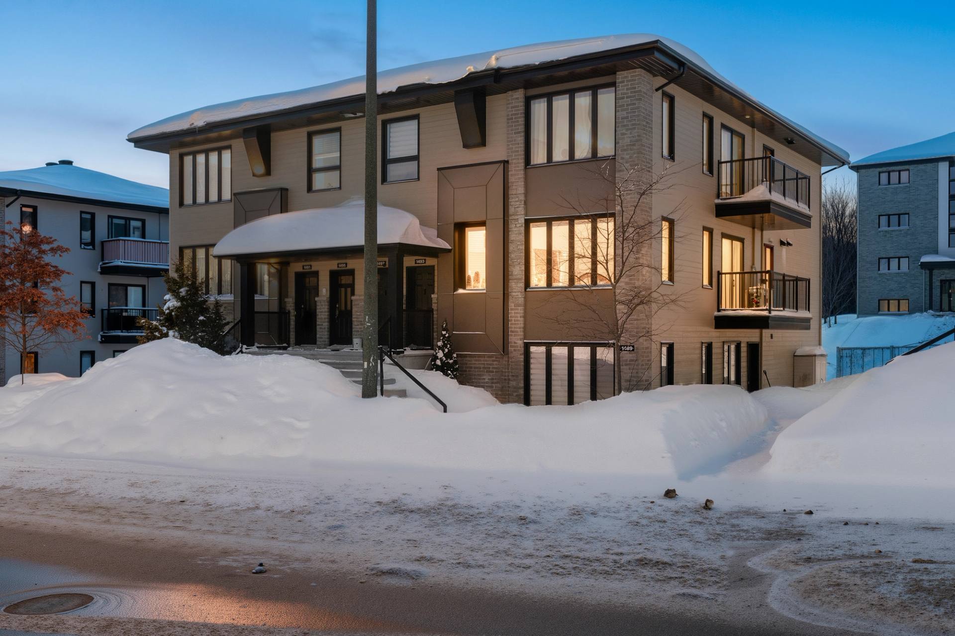 Immeuble résidentiel de trois étages photographié en hiver, fenêtres éclairées et bancs de neige
