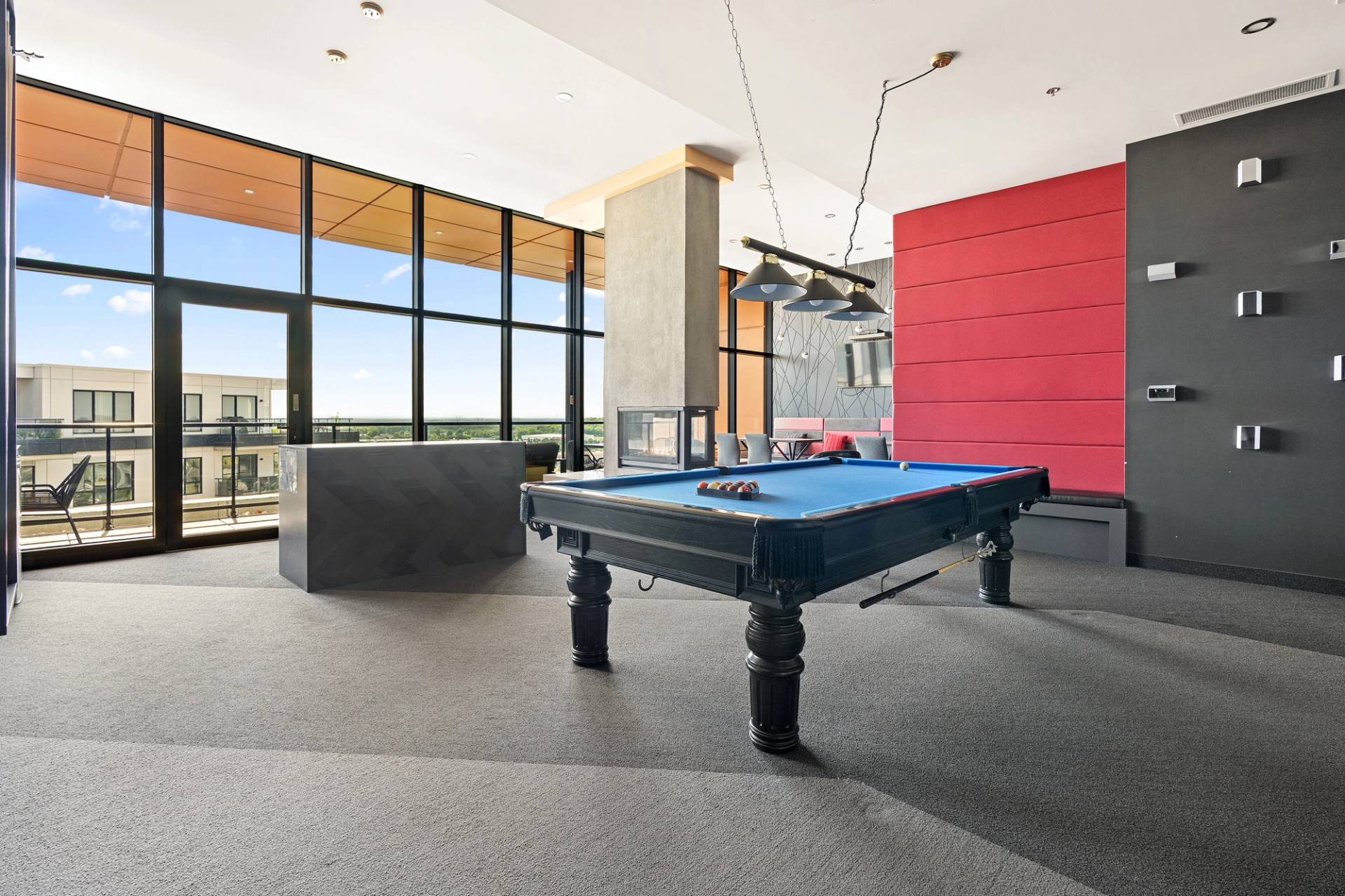 Salle de jeux d'un immeuble avec table de billard, mur rouge et fenêtres pleine hauteur