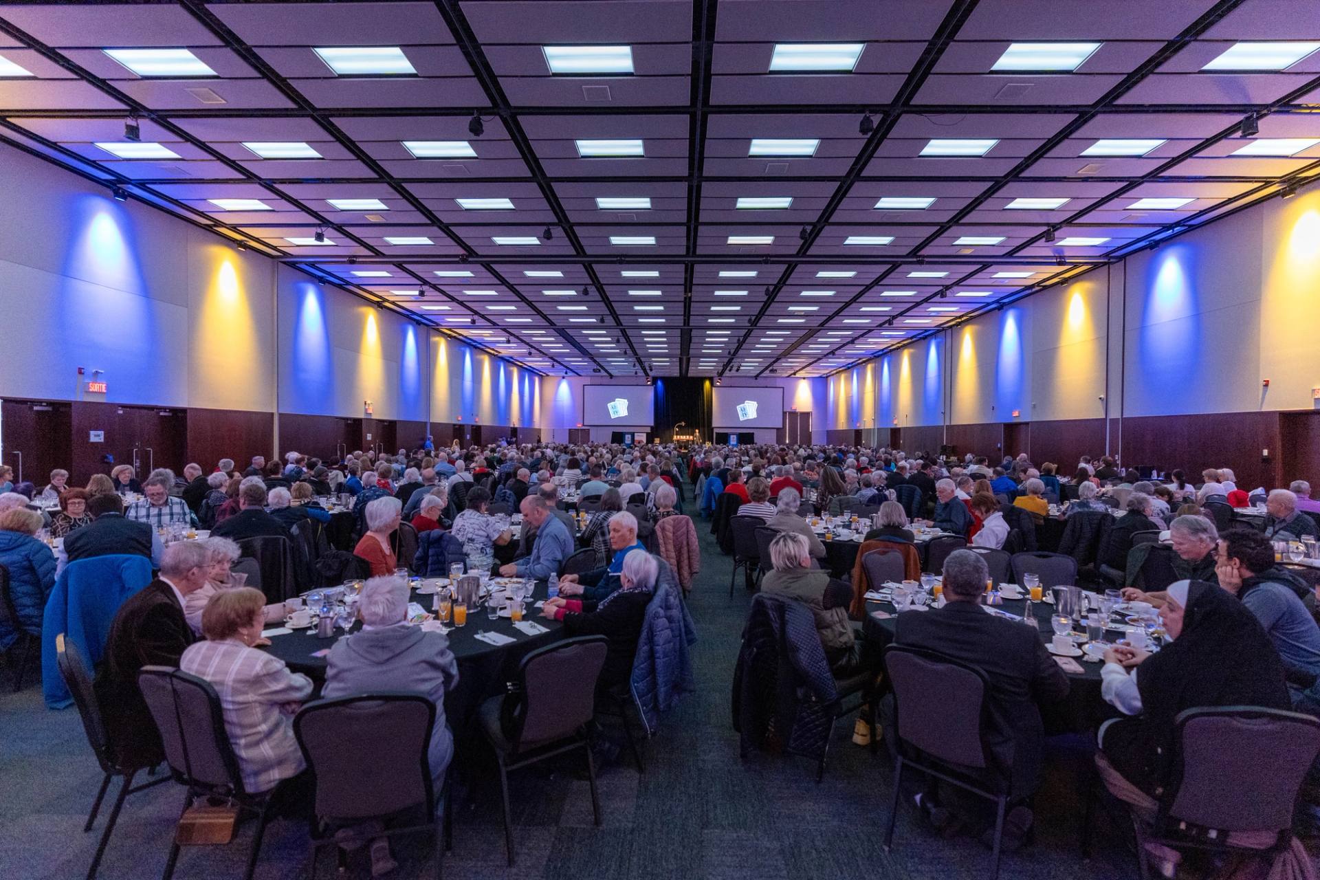 Grande salle de banquet aux tables dressees, eclairage bleu et violet, avant l'arrivee des invites