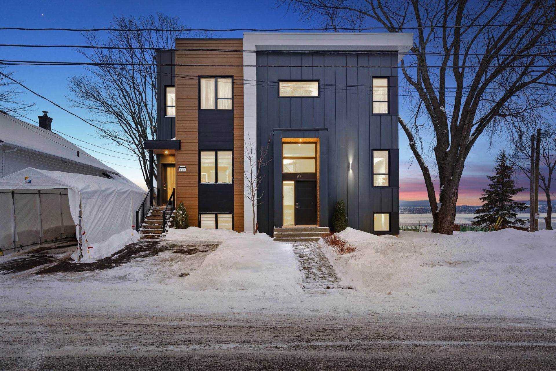 Façade d'un duplex contemporain photographiée au crépuscule en hiver, ciel rosé au-dessus du fleuve