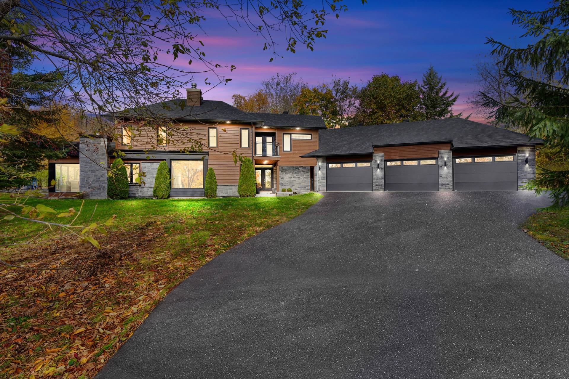 Façade d'une résidence de deux étages éclairée au crépuscule, garage double et longue allée pavée