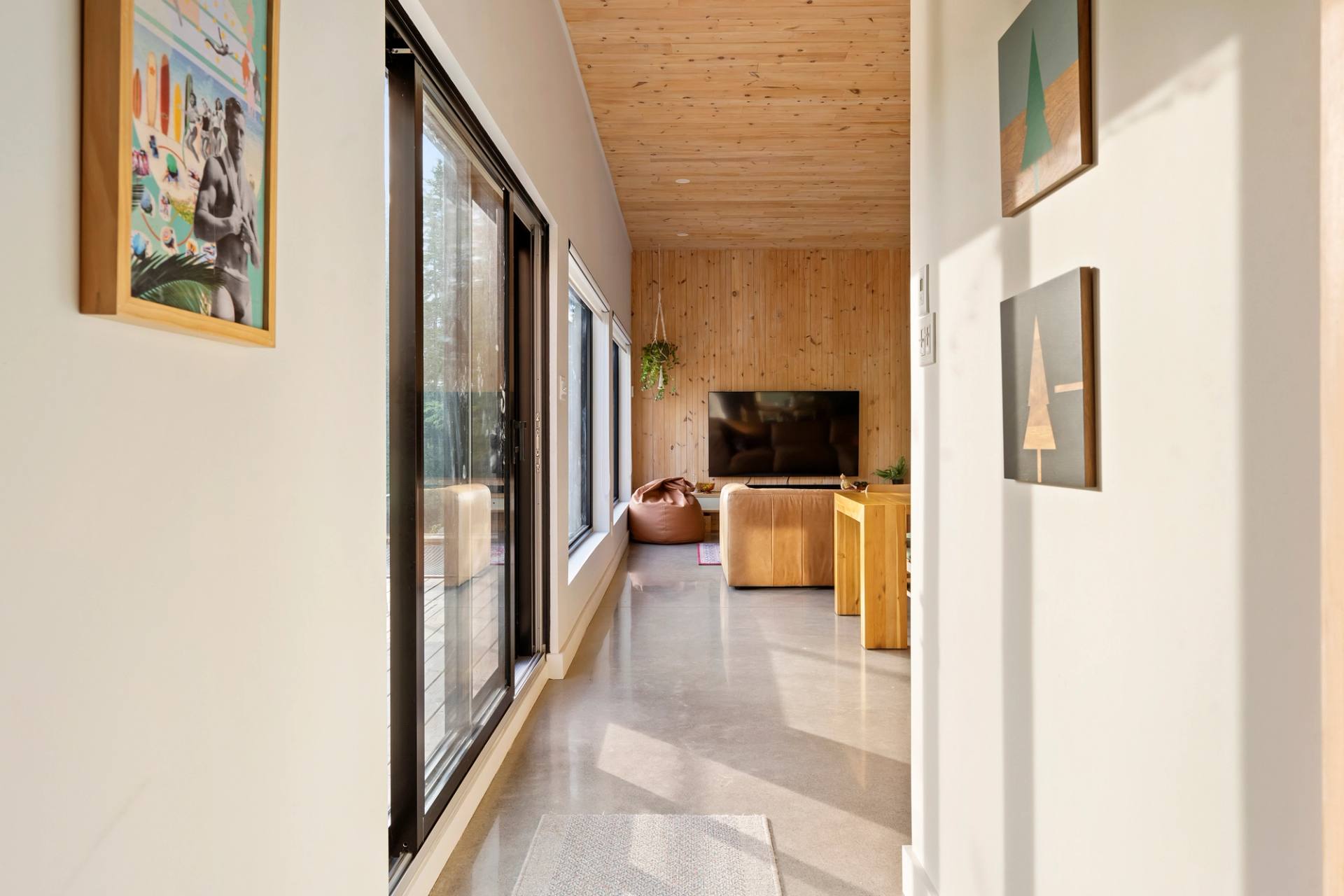 Sejour a aire ouverte sous un plafond cathedrale en bois clair, grandes fenetres sur la foret