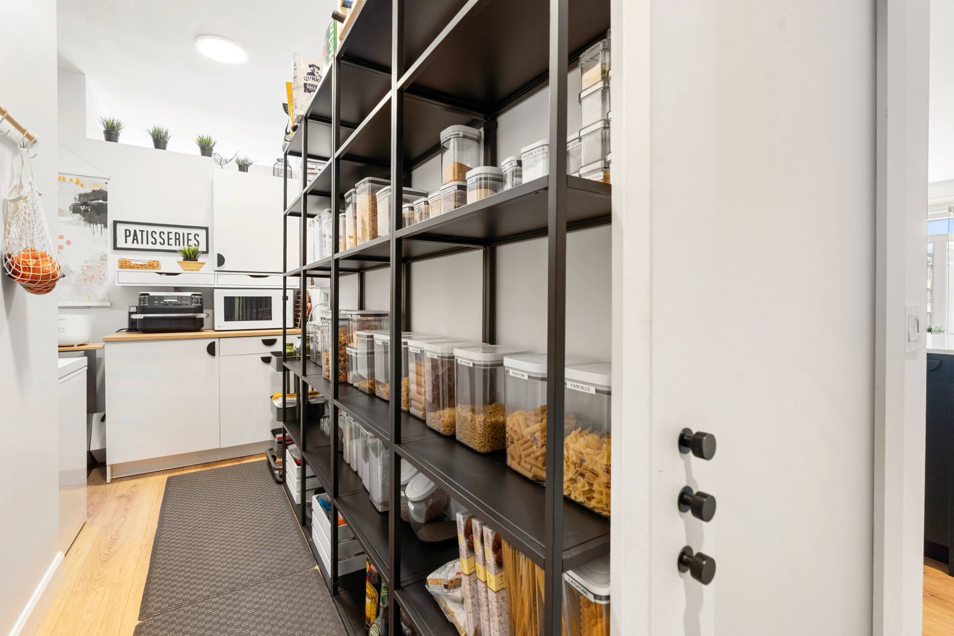Garde-manger avec étagères de métal noir garnies de bocaux, le long d'un corridor