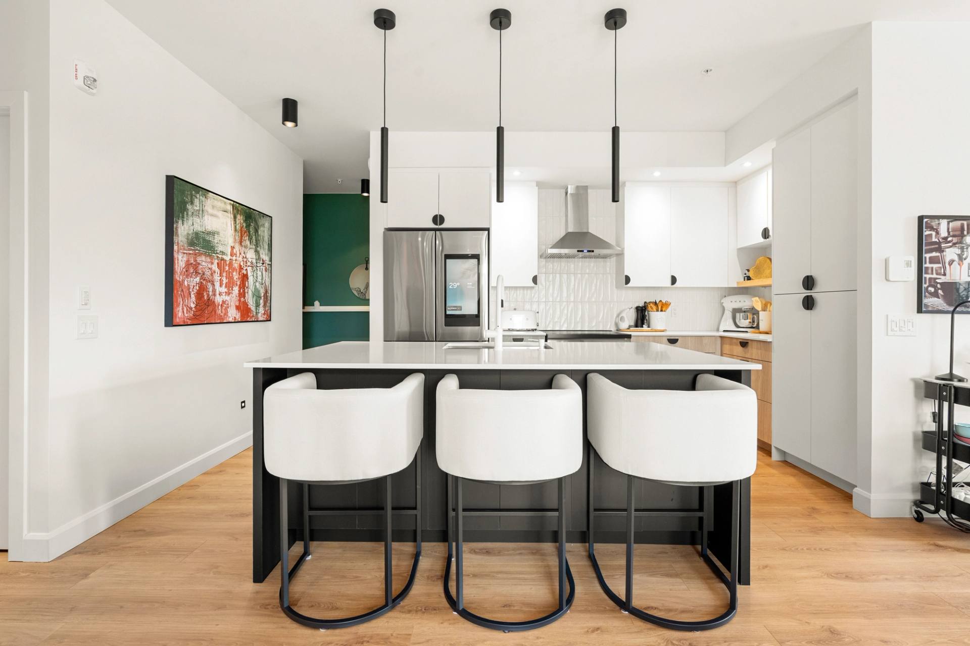 Cuisine blanche avec îlot central, trois tabourets noirs et blancs et plancher de bois clair