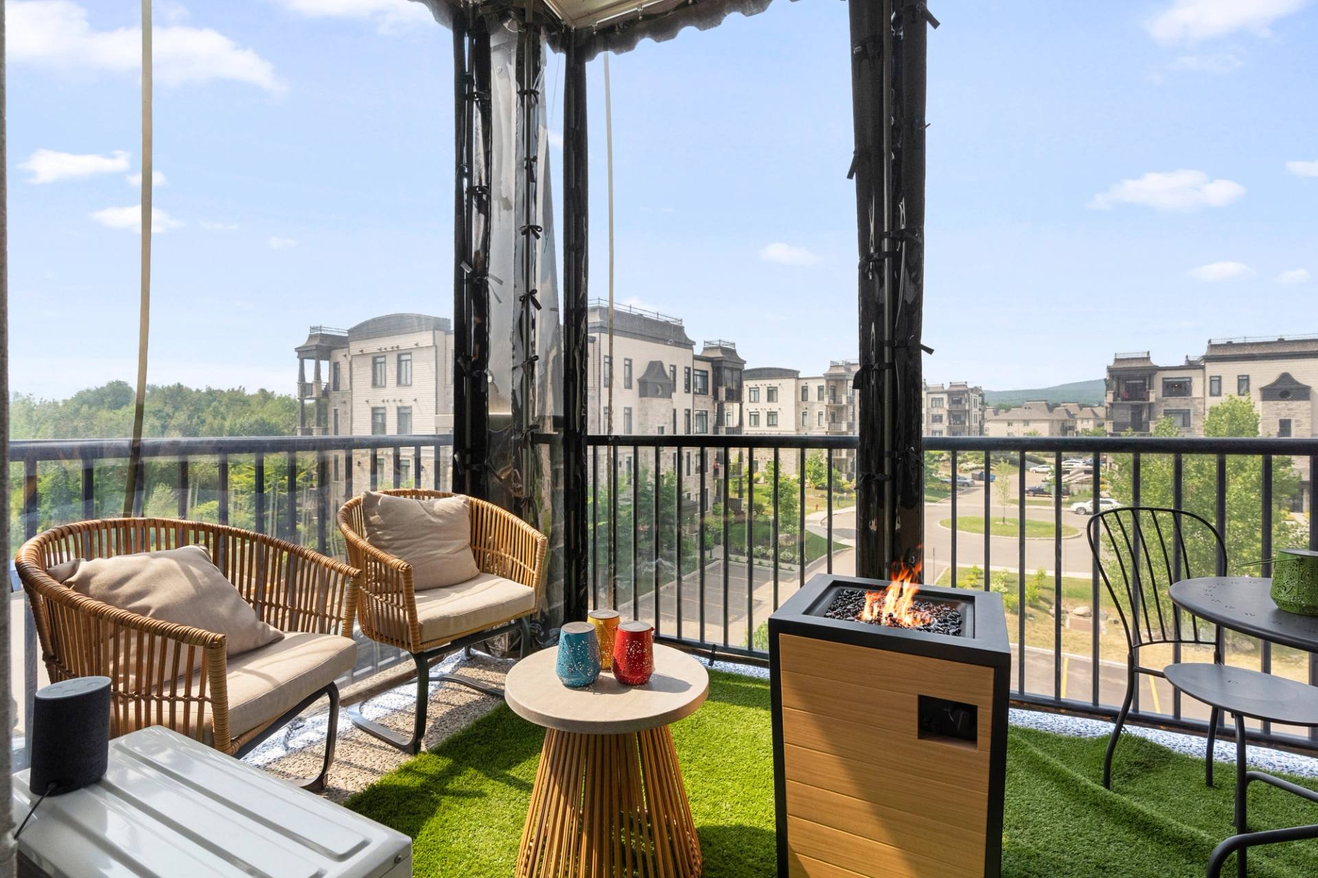 Balcon aménagé avec foyer extérieur, fauteuils de rotin et gazon synthétique, vue sur le quartier