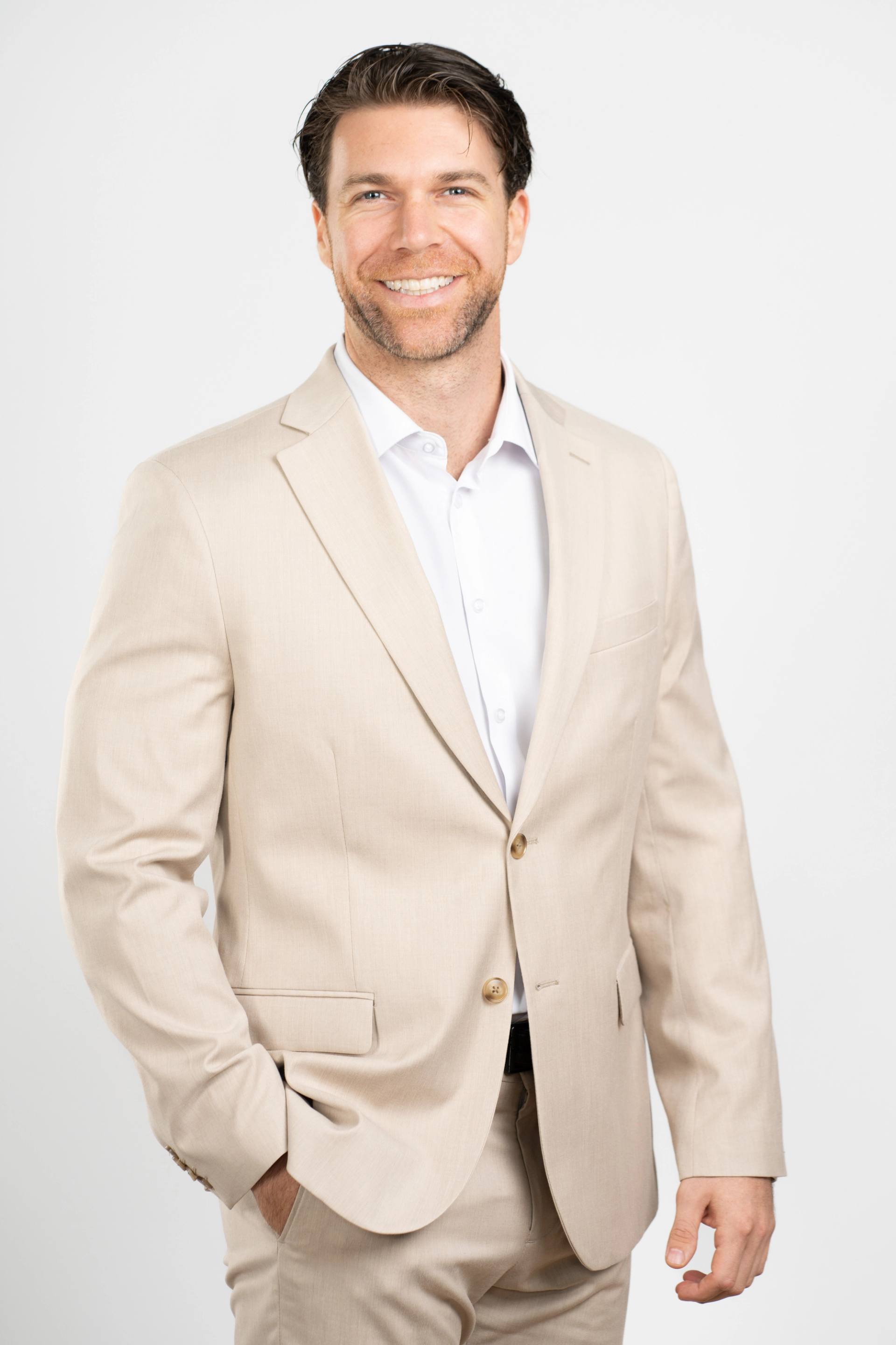 Portrait d'un homme en veston beige et chemise blanche, bras croises