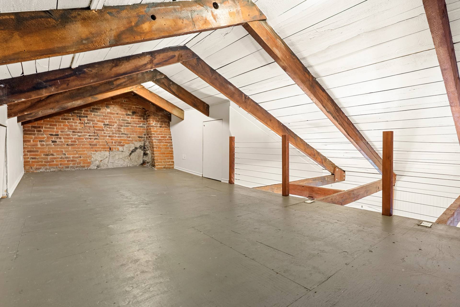 Grenier vide au plancher de béton, murs de brique et poutres de bois apparentes