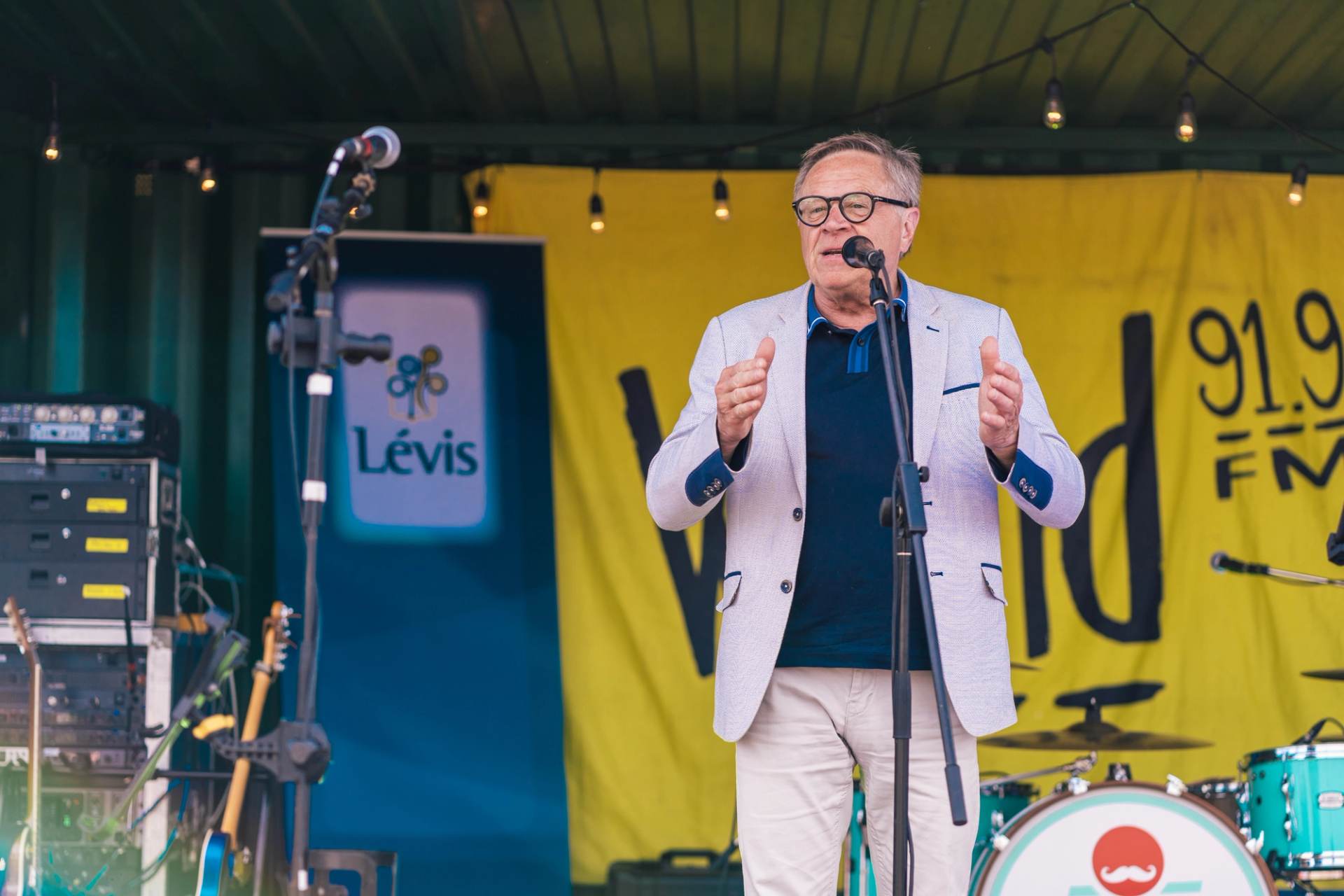 Animateur au micro sur la scene de la fete des benevoles de Levis, banniere de la ville en arriere-plan
