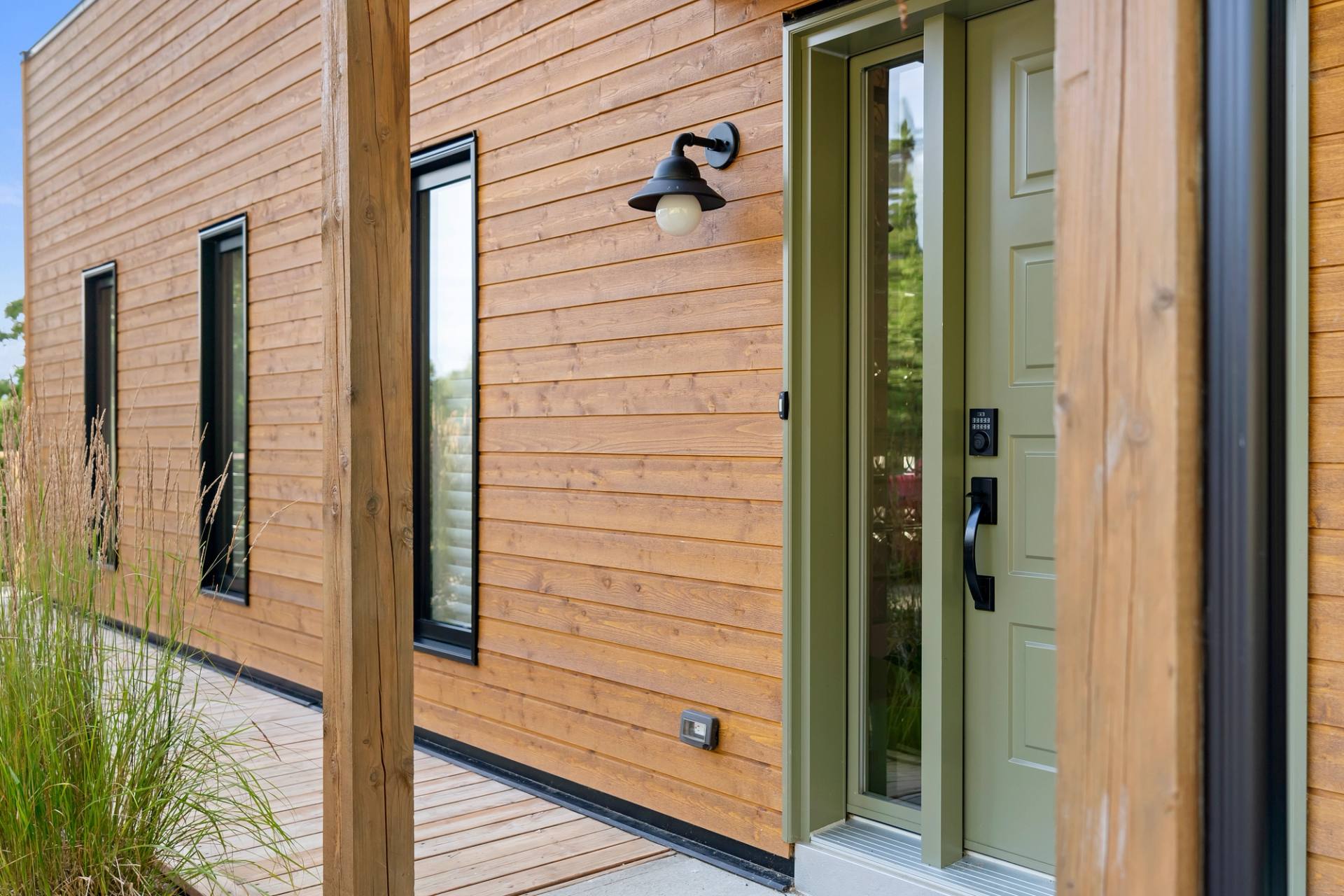 Facade du chalet au bardage vert et porte vitree, sous les arbres