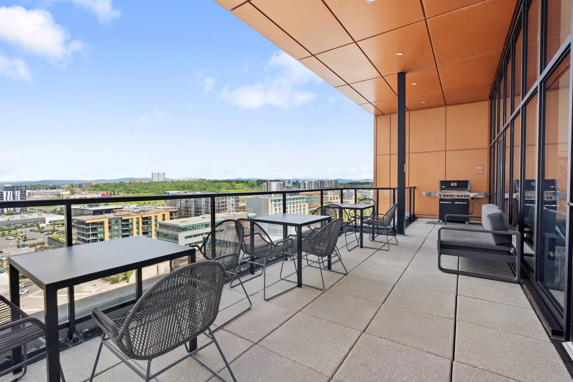 Terrasse sur le toit d'un immeuble, tables et chaises sous un plafond de bois, vue sur la ville