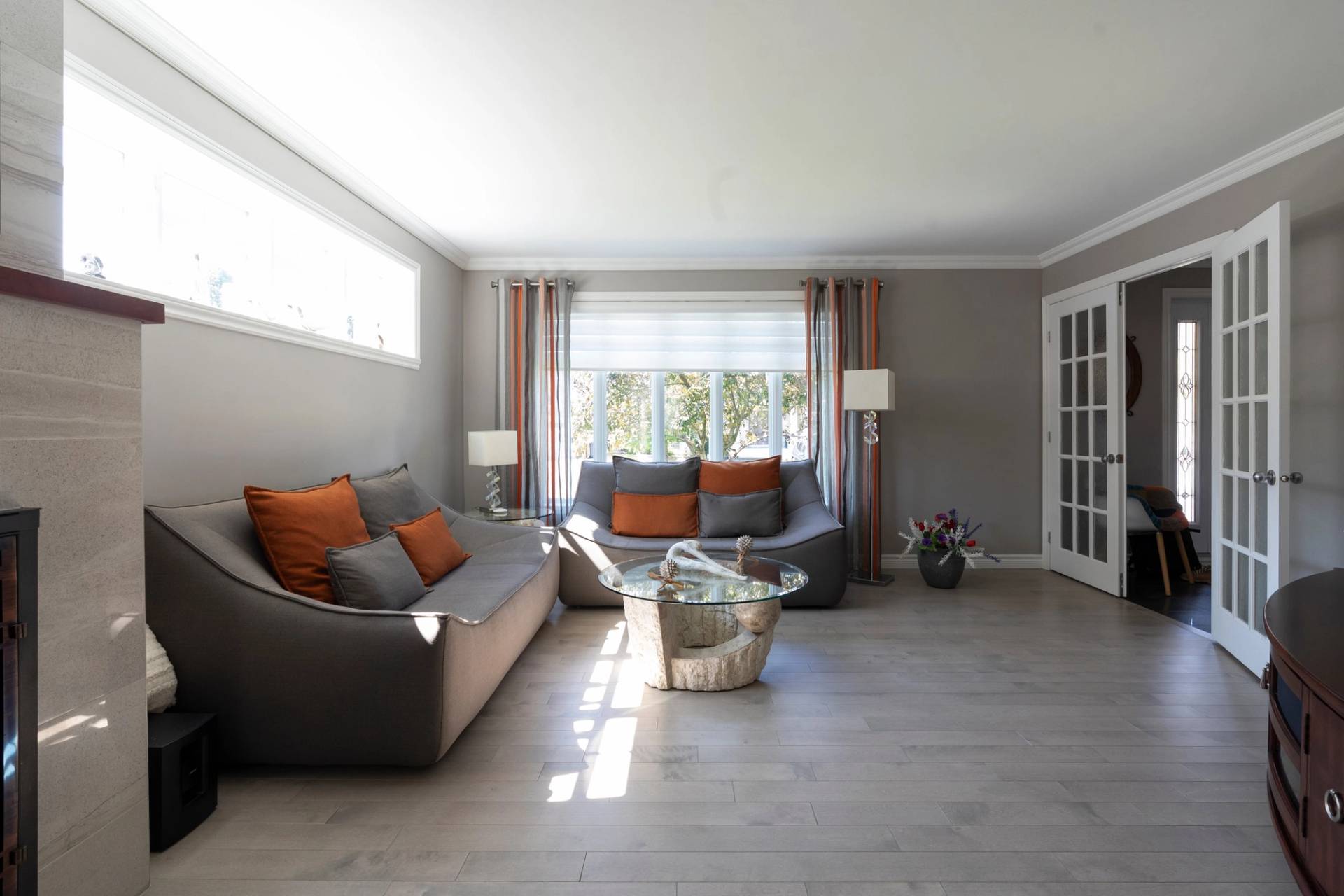 Salon gris avec canapés et coussins orange, fenêtre haute entièrement blanche sous le plafond
