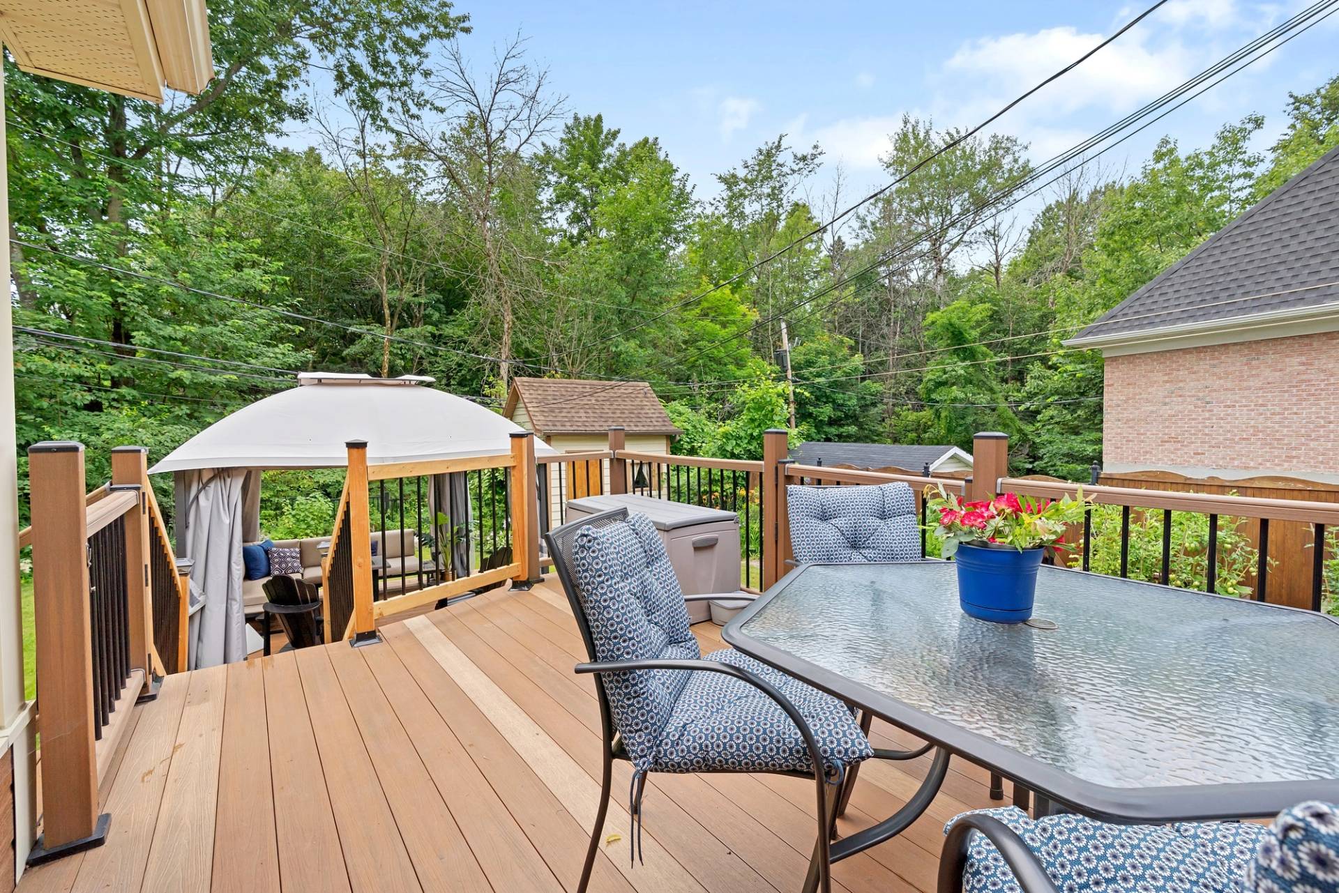 La même terrasse sous un ciel bleu nuageux, le boisé bien vert derrière le gazebo