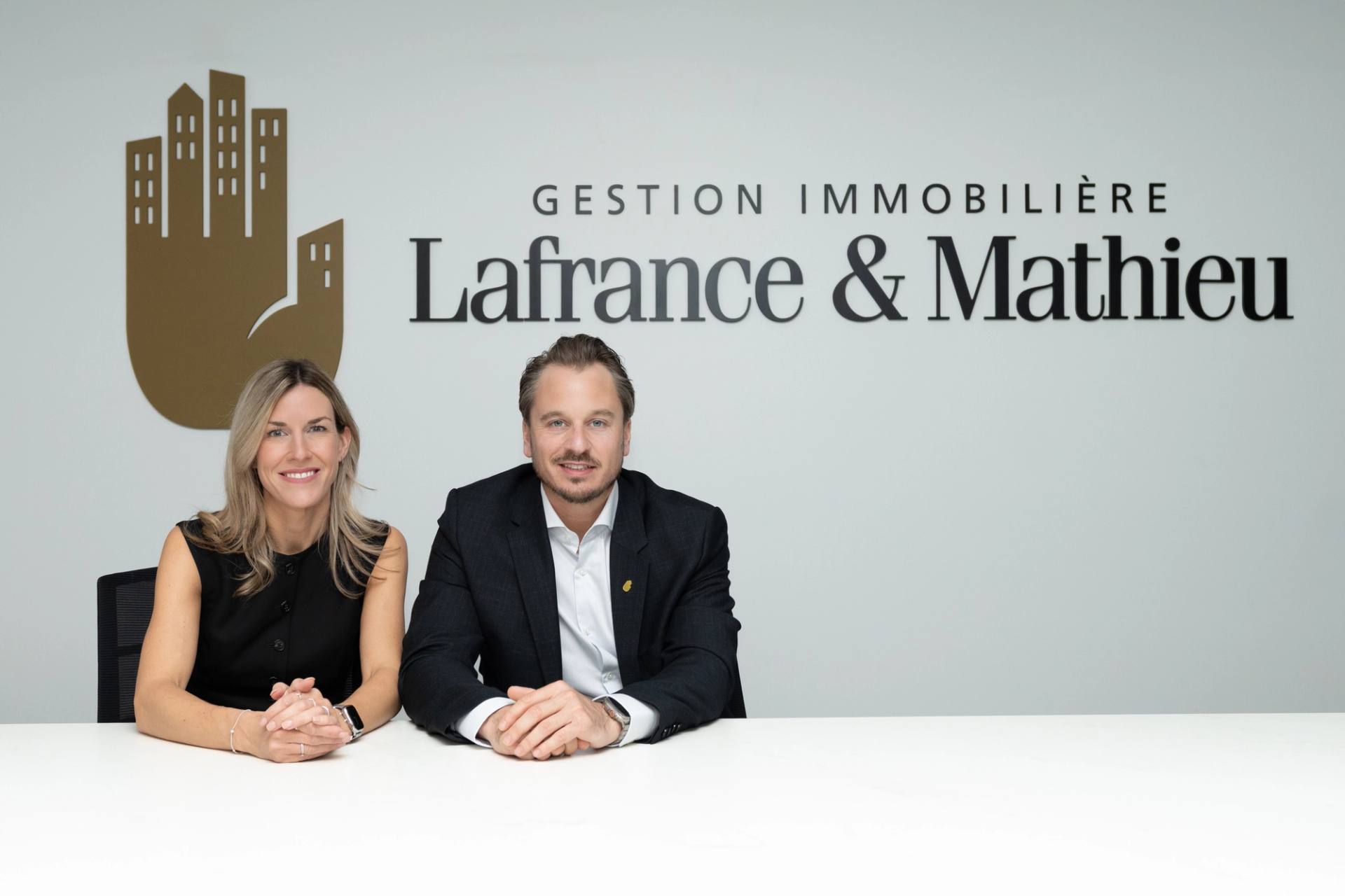 Duo de courtiers assis devant l'enseigne de Gestion immobiliere Lafrance et Mathieu