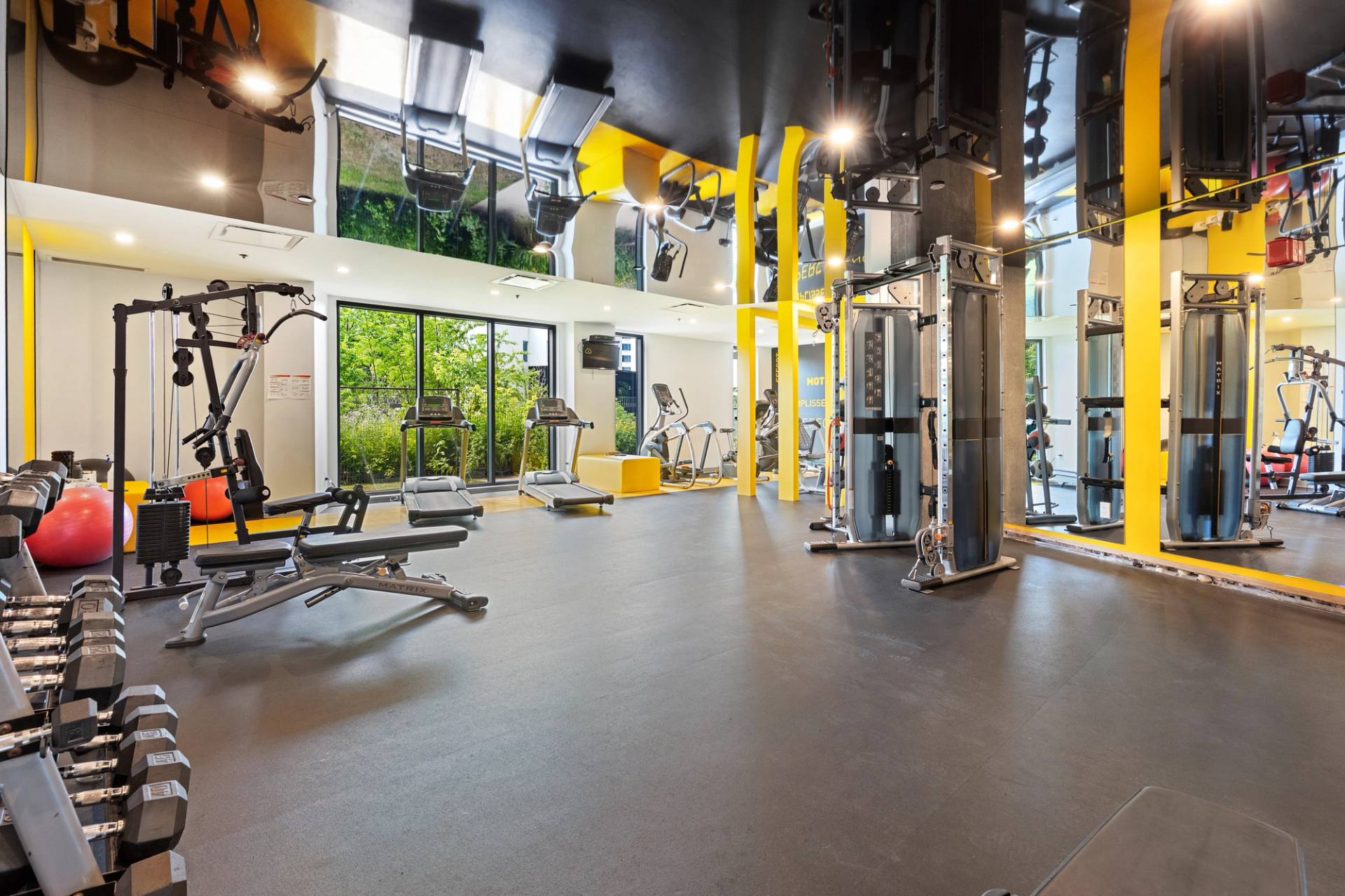 Salle d'entraînement d'un immeuble résidentiel, appareils de musculation et grandes fenêtres