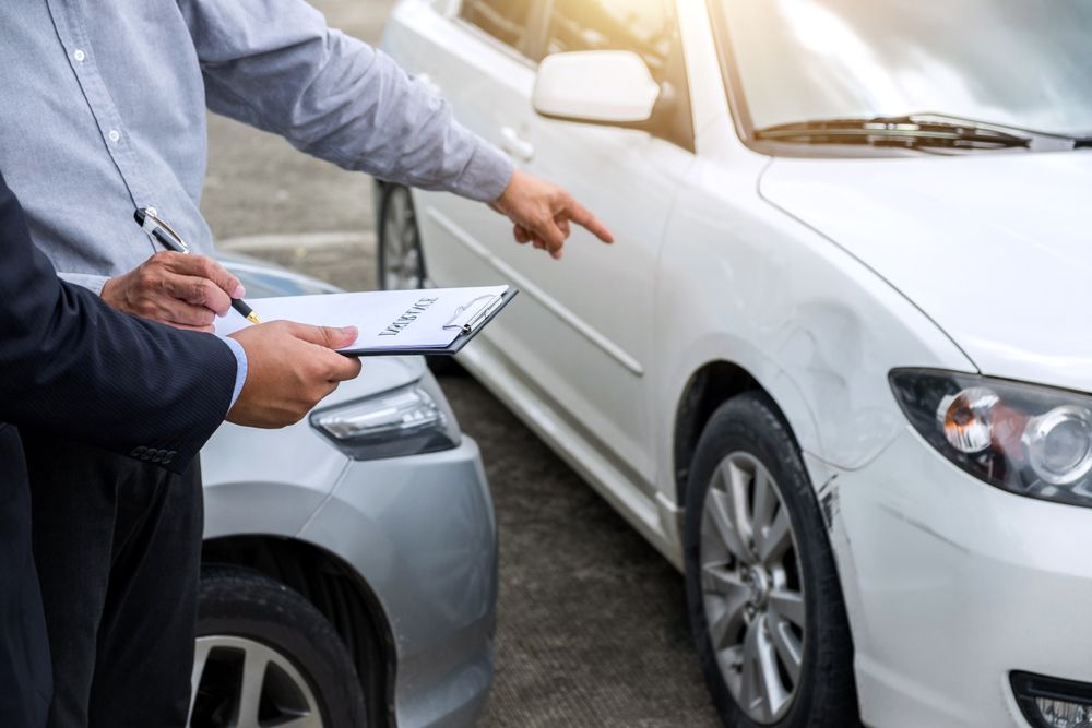 Insurance adjuster inspecting vehicle damage after a car accident and taking notes for an Erie County auto insurance claim.