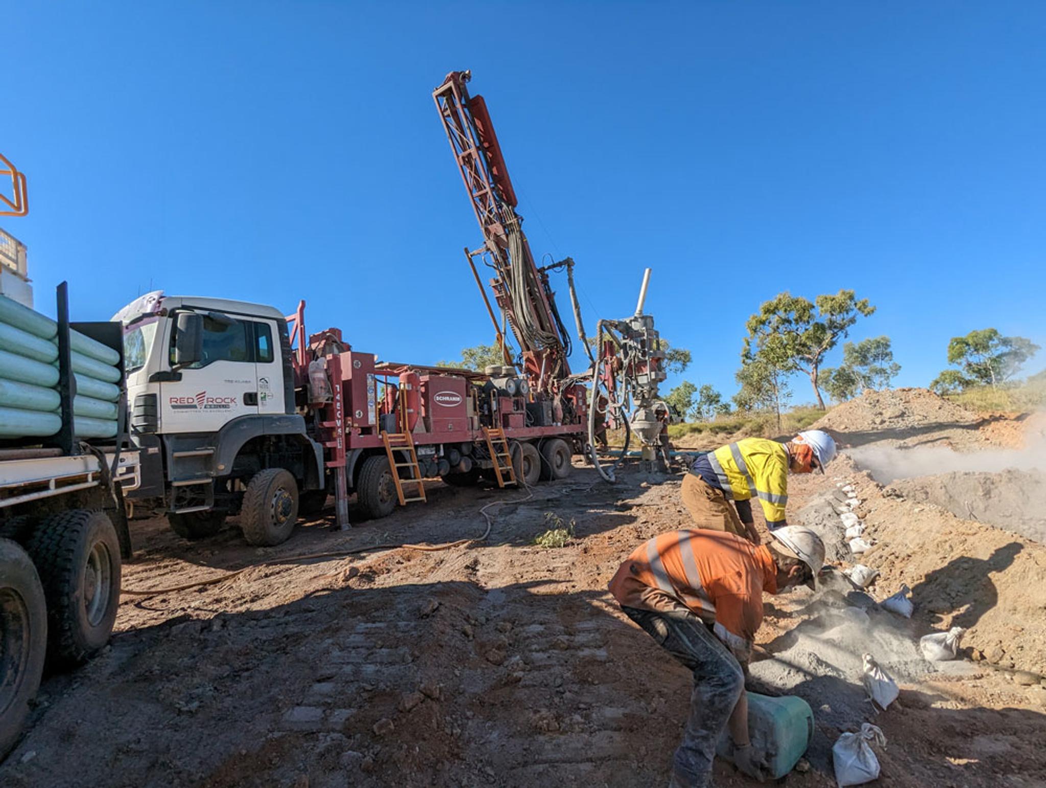 men working in the bush, crane on flatbed truck in the background