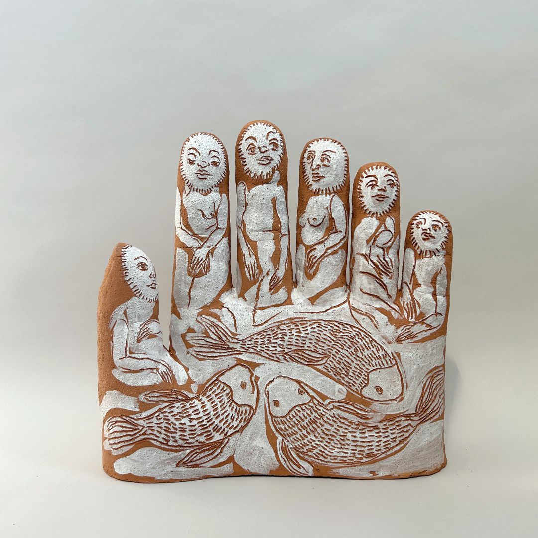 Terracotta ceramic hand sculpture with white-glazed figures carved onto each finger and koi fish on the palm.