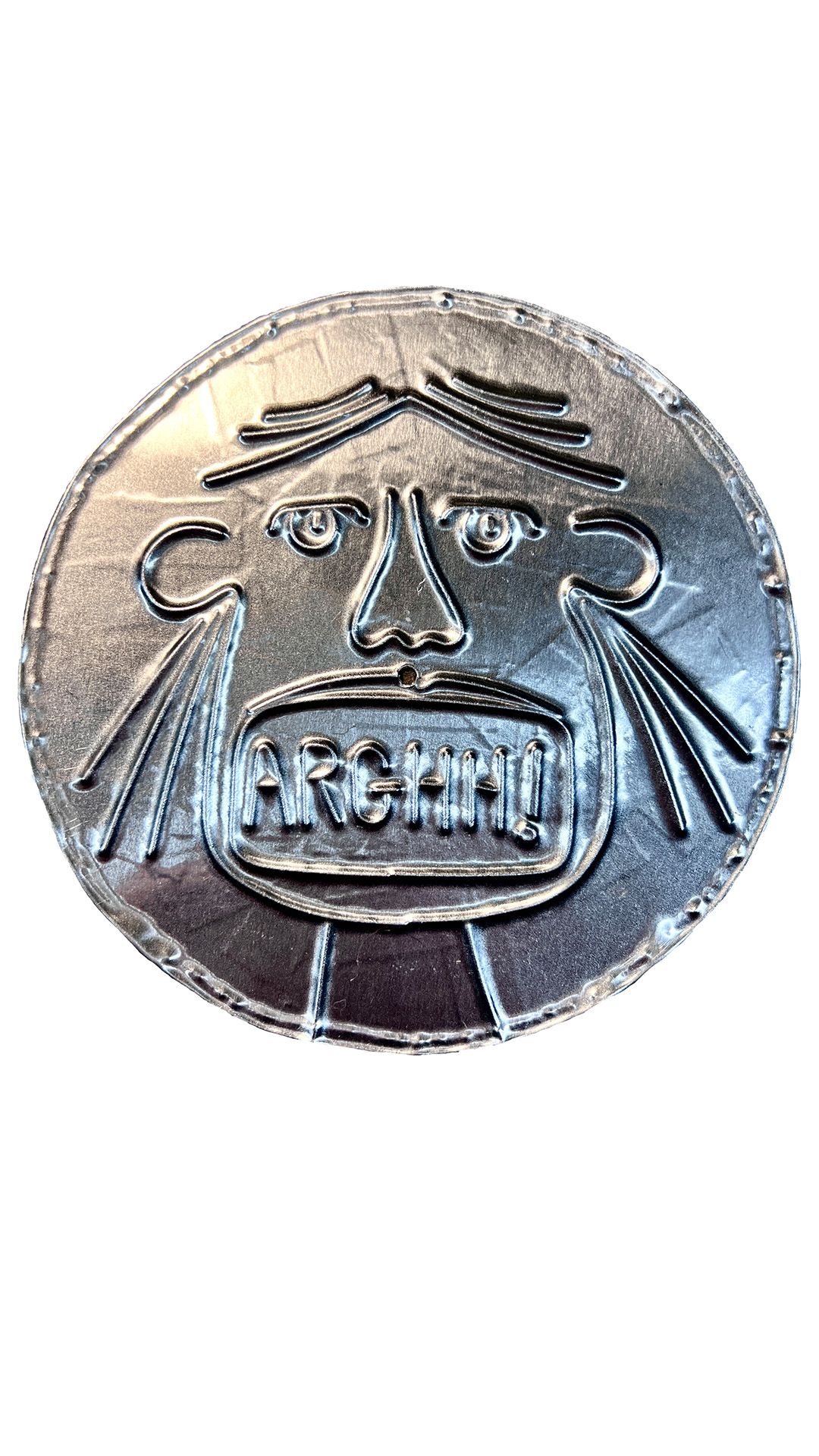 Circular embossed metal disc with a grimacing face and the word "ARGHH!" pressed into the mouth area, on a white background.