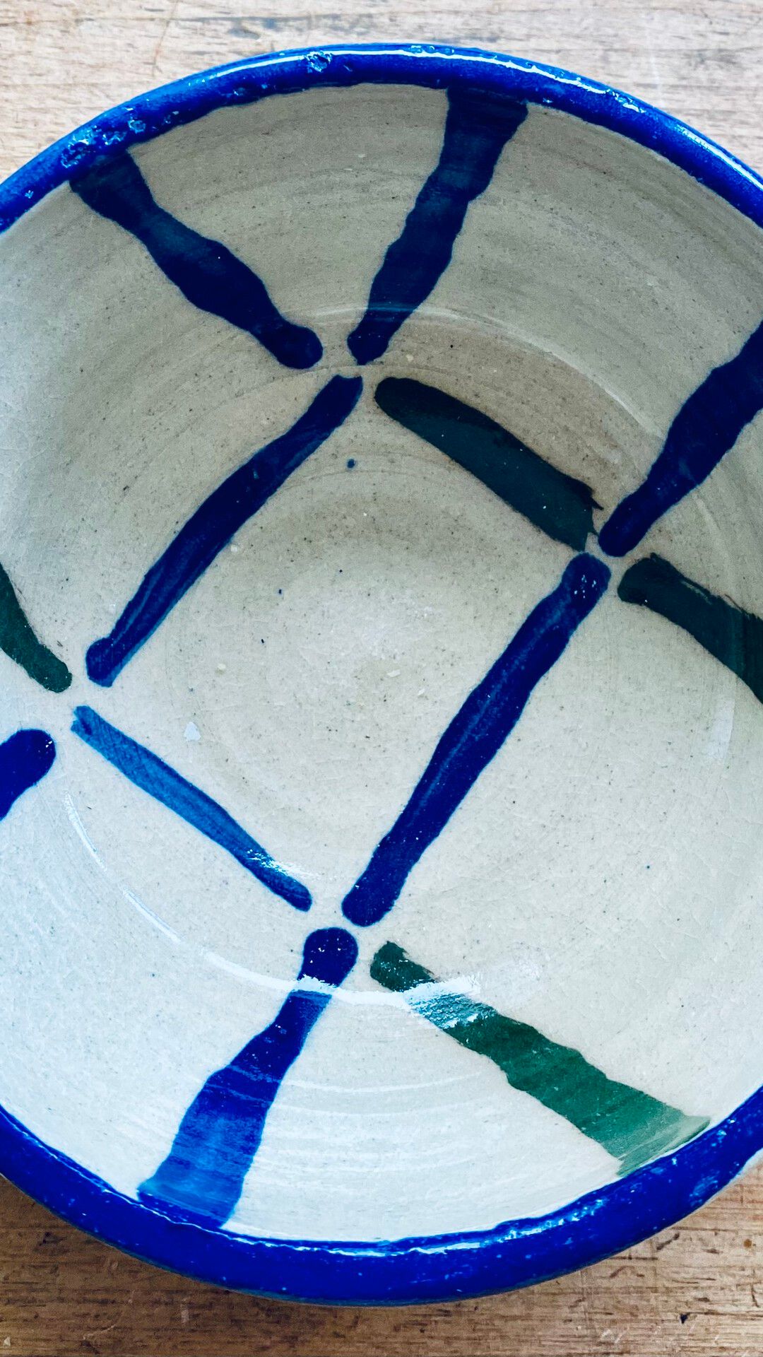 Handmade ceramic bowl with a cobalt blue rim and loosely painted blue and green stripe pattern inside, on a wooden surface.