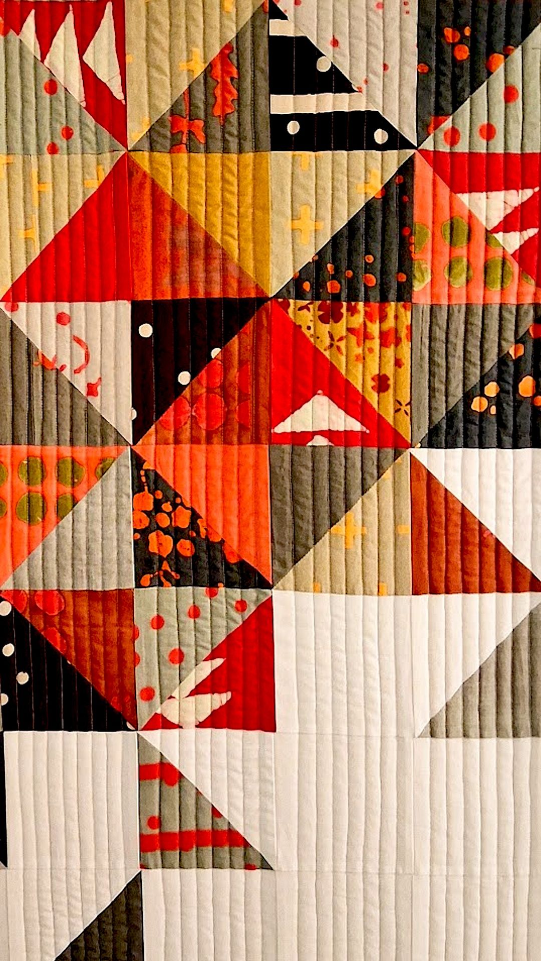 Close-up of a geometric quilt with bold triangular blocks in red, orange, black and grey, some panels with splattered print fabric.