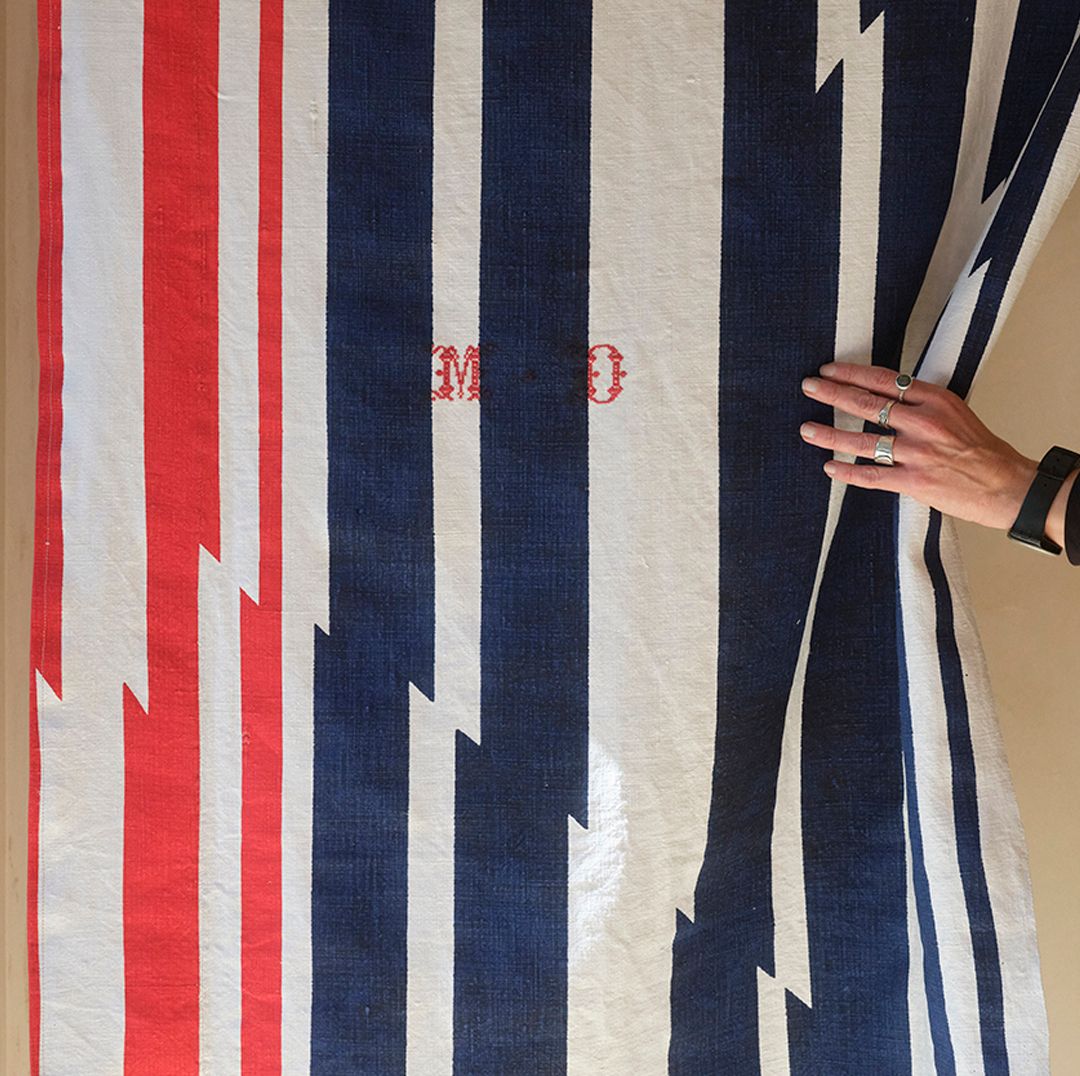 Striped red, navy and cream fabric with zigzag stripe ends, embroidered letters, held up by a hand wearing rings.