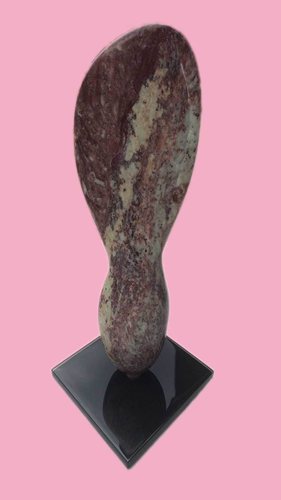 Polished granite sculpture in an organic, hourglass-like shape with mottled purple-grey patterning, on a black base, pink backdrop.
