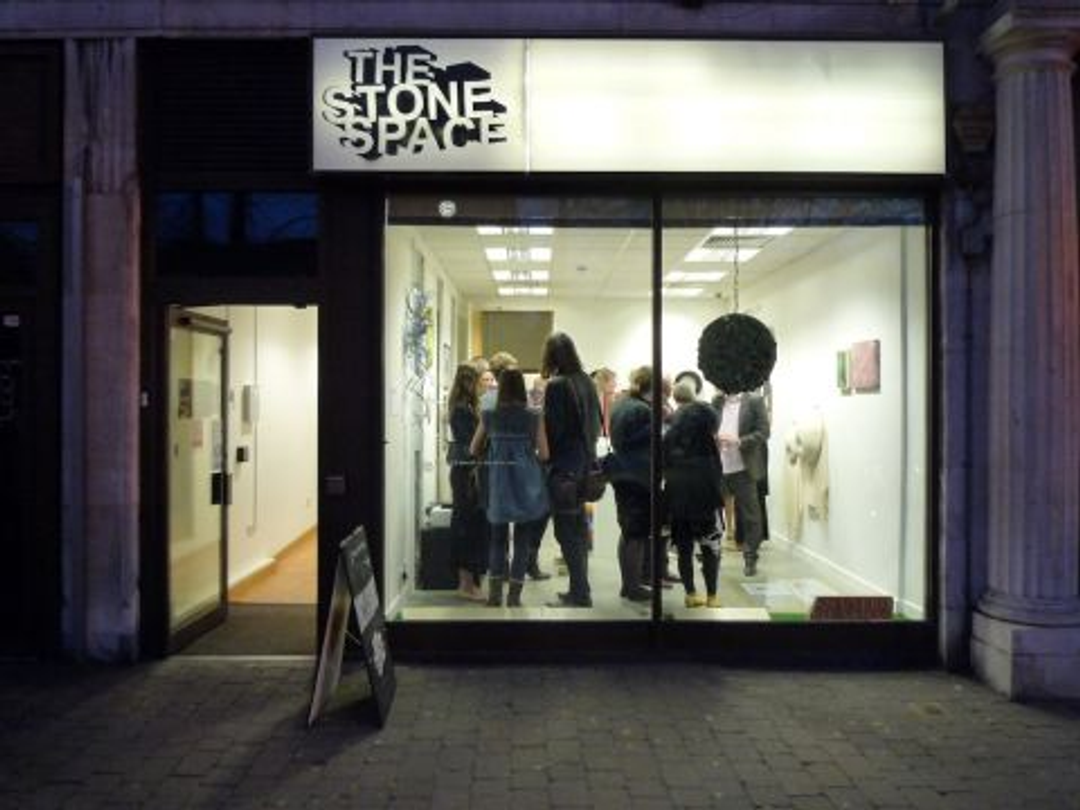 A street view of The Stone Space gallery, showing a group of people enjoying an evening event hosted by the artist and gallery volunteers. The picture shows the gallery is accessible and welcoming.