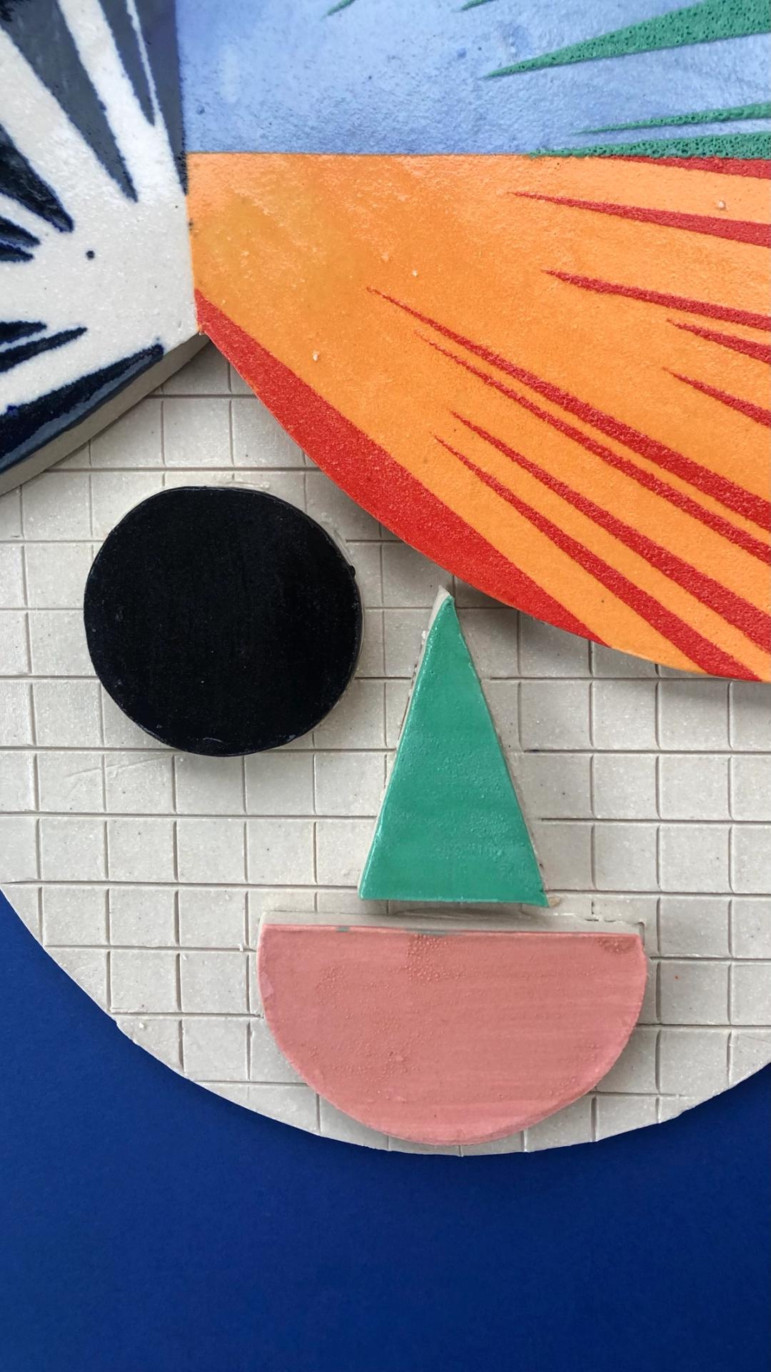 Ceramic tile artwork with bold geometric shapes — black circle, green triangle, pink semicircle — against an orange and blue background.