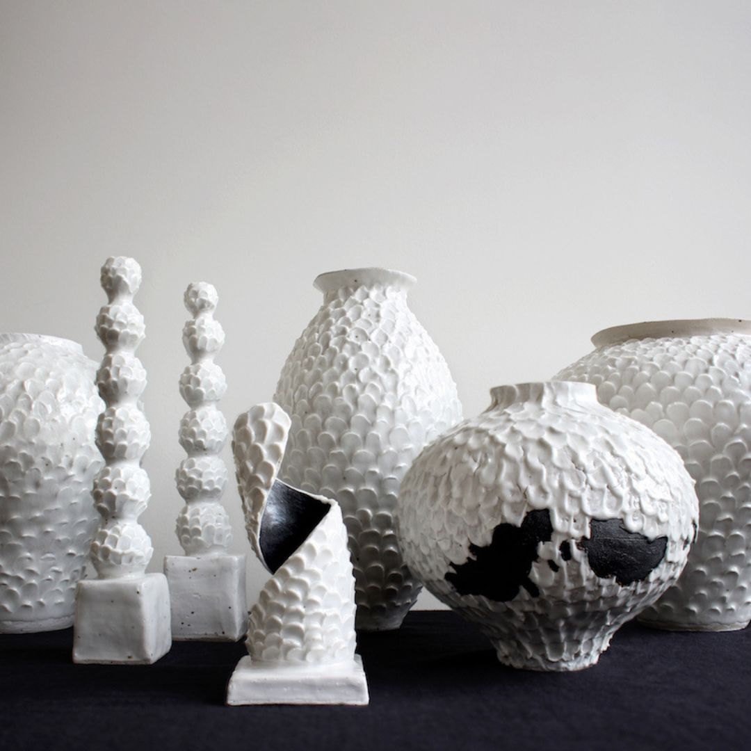 Still life group image of multiple black and white ceramic vessels with textured surfaces.