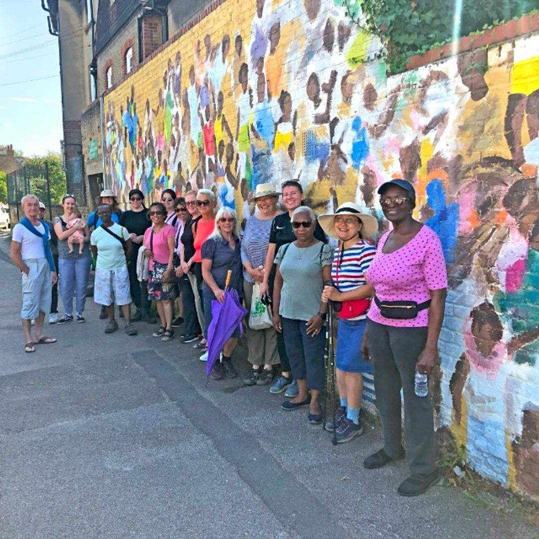 A picture of members of the walking group next to the mural by Paul Dash on the wall of the Good Shepherd building in Davies Lane