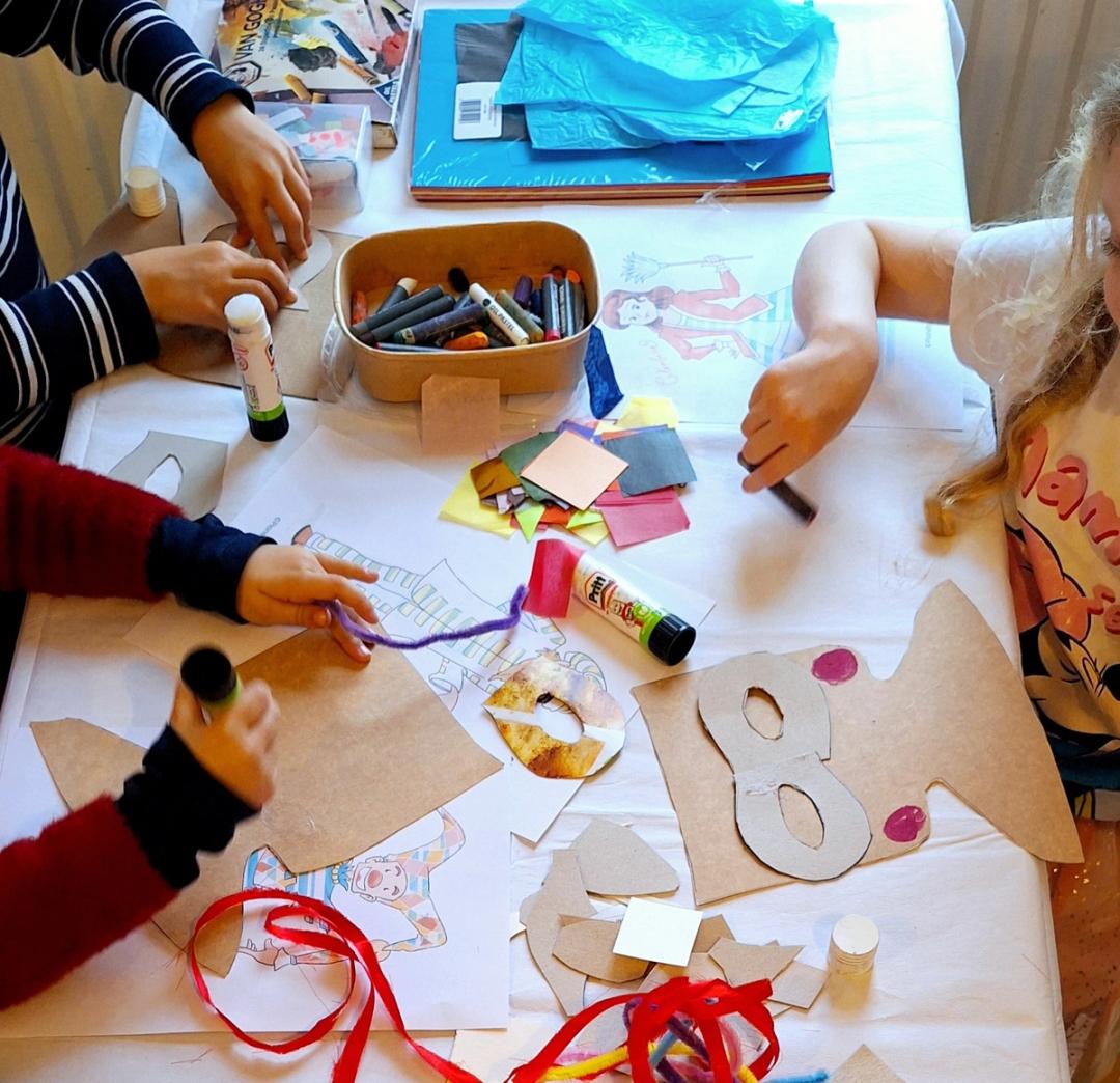 "Children around the table making art with their hands. There are colourful materials and tools on the table