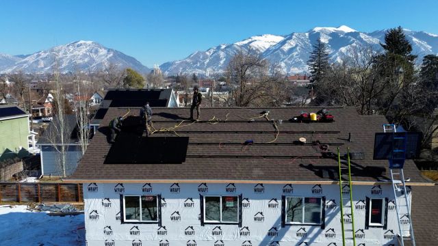 Green Box Solar crew installing rooftop panels with snow-capped mountains behind