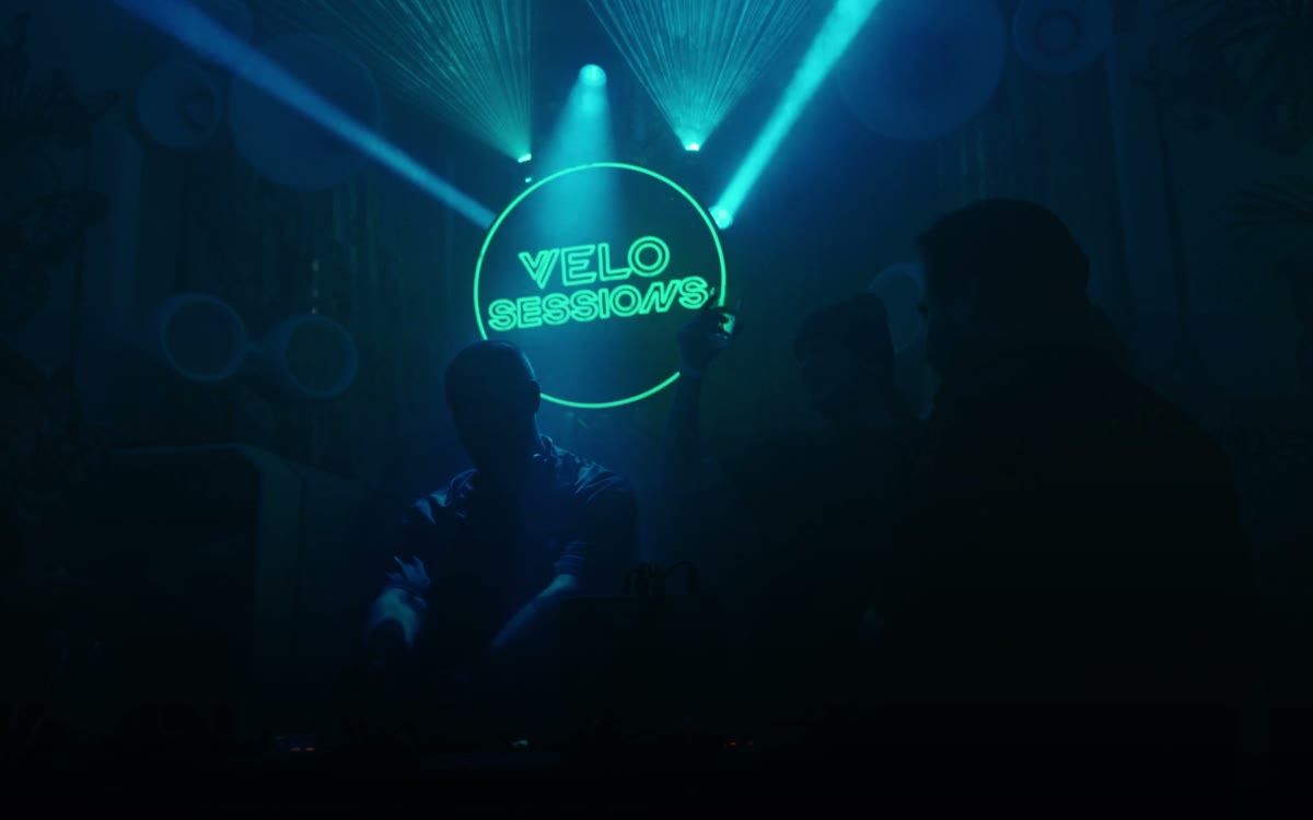 Neonskylt med texten VELO Sessions över DJ-bås