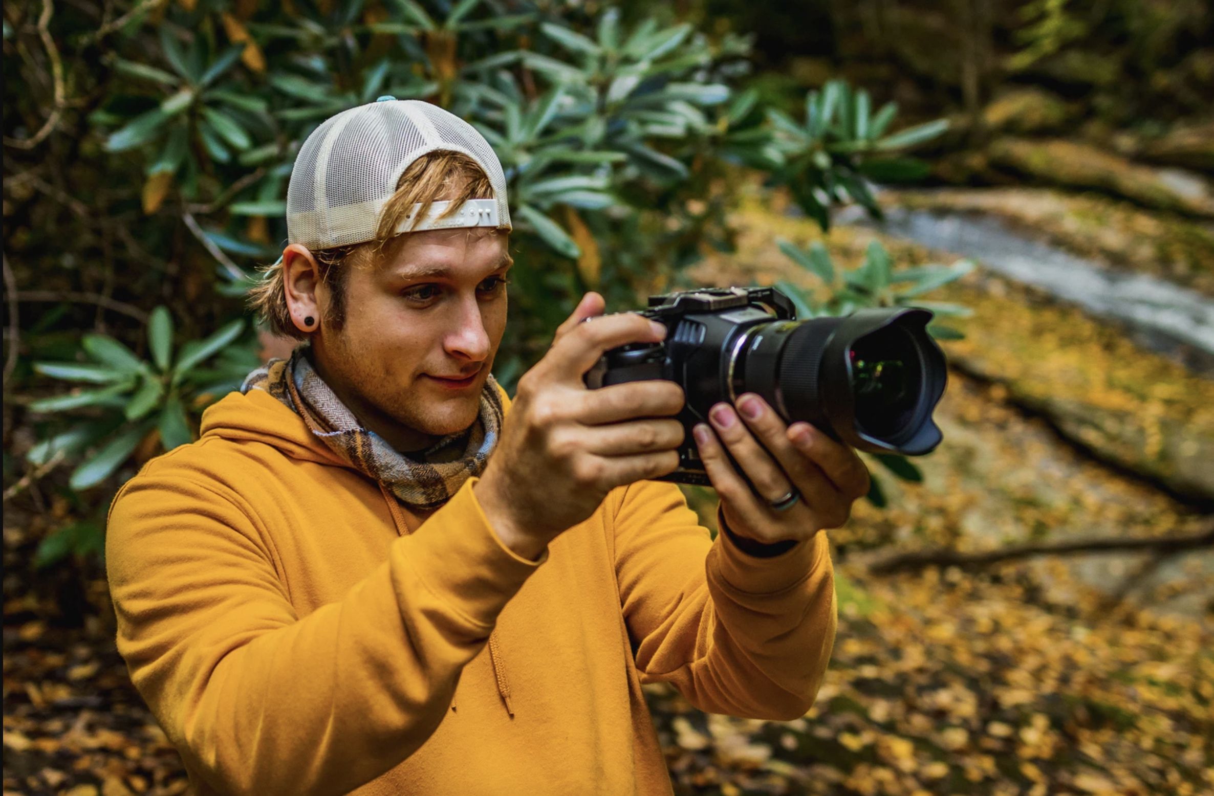 A young man holding a camera in nature.