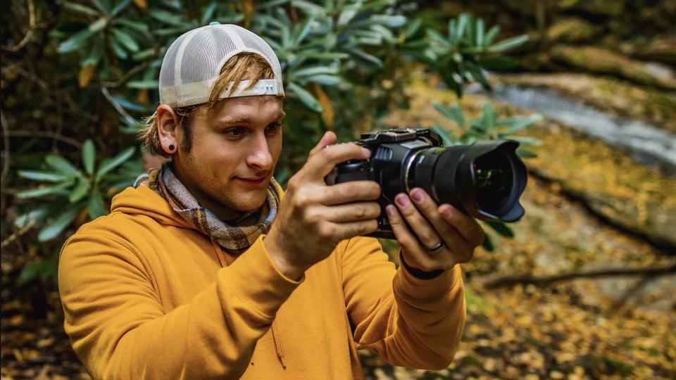 A young man holding a camera in nature.