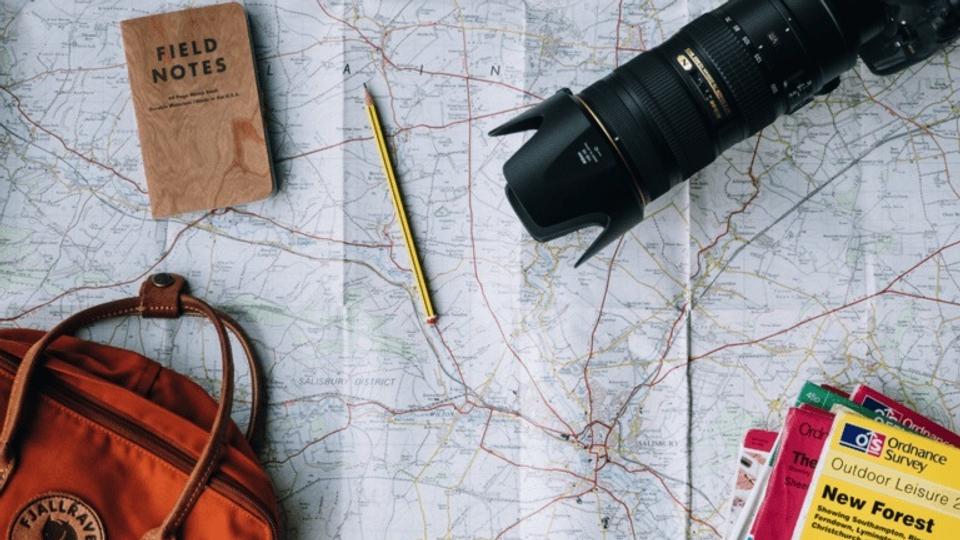 A camera, notebook, and pencil laid out on top of a map.