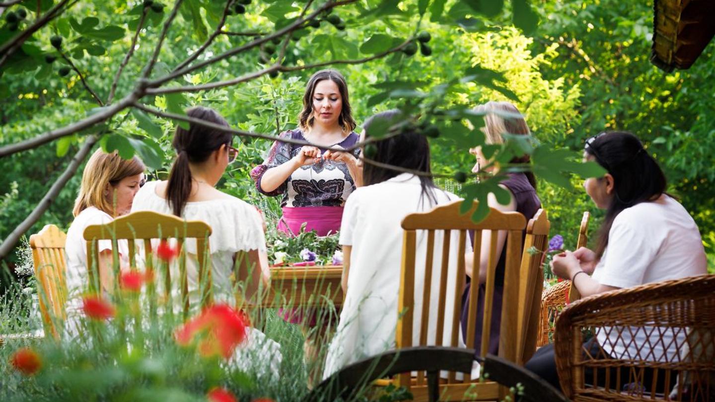 A woman leading a culinary retreat session around a table in a garden.