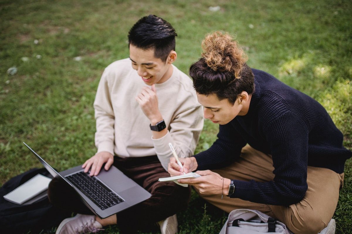 Two people sitting on the grass using a laptop to look for booking systems.