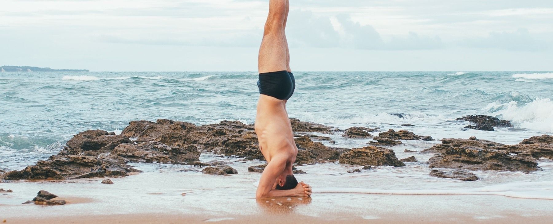 A man doing a headstand on the beach during a yoga retreat.