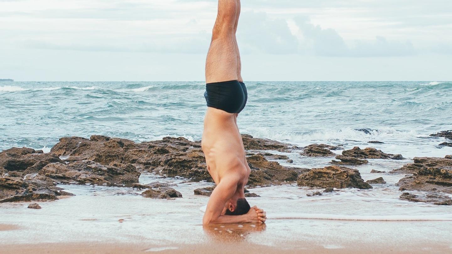 A man doing a headstand on the beach during a yoga retreat.