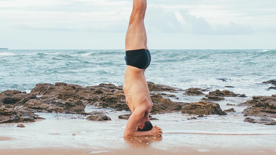 A man doing a headstand on the beach during a yoga retreat.