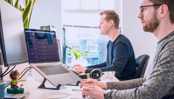 Two men working at a desk on computers and laptops