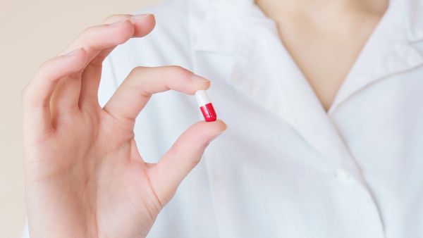 close up picture of woman holding small red and white capsule pill