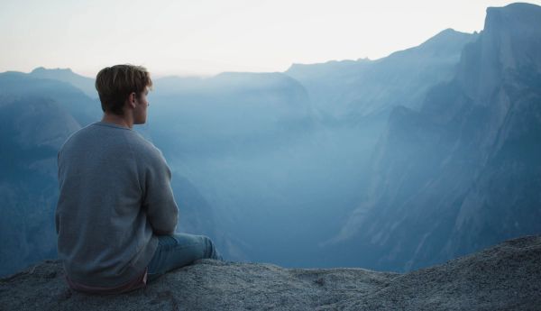 Man sitting on edge of cliff looking into the distance lost in thought