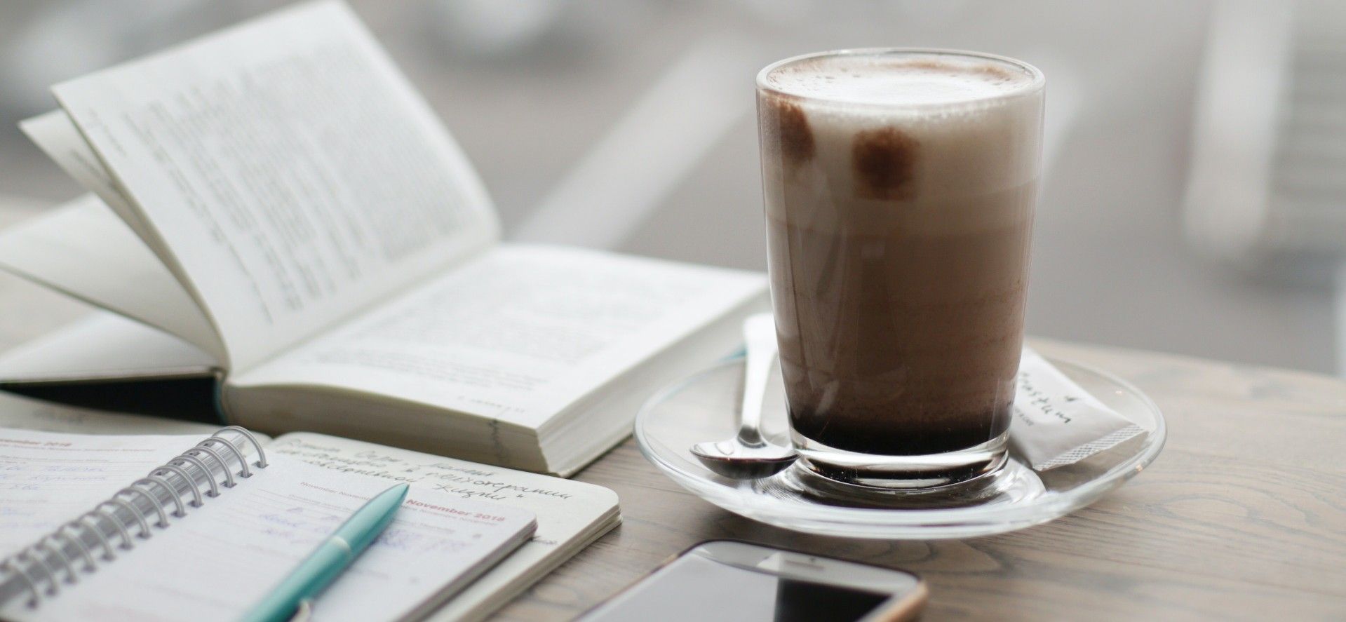 Frothy glass of coffee beside an open book