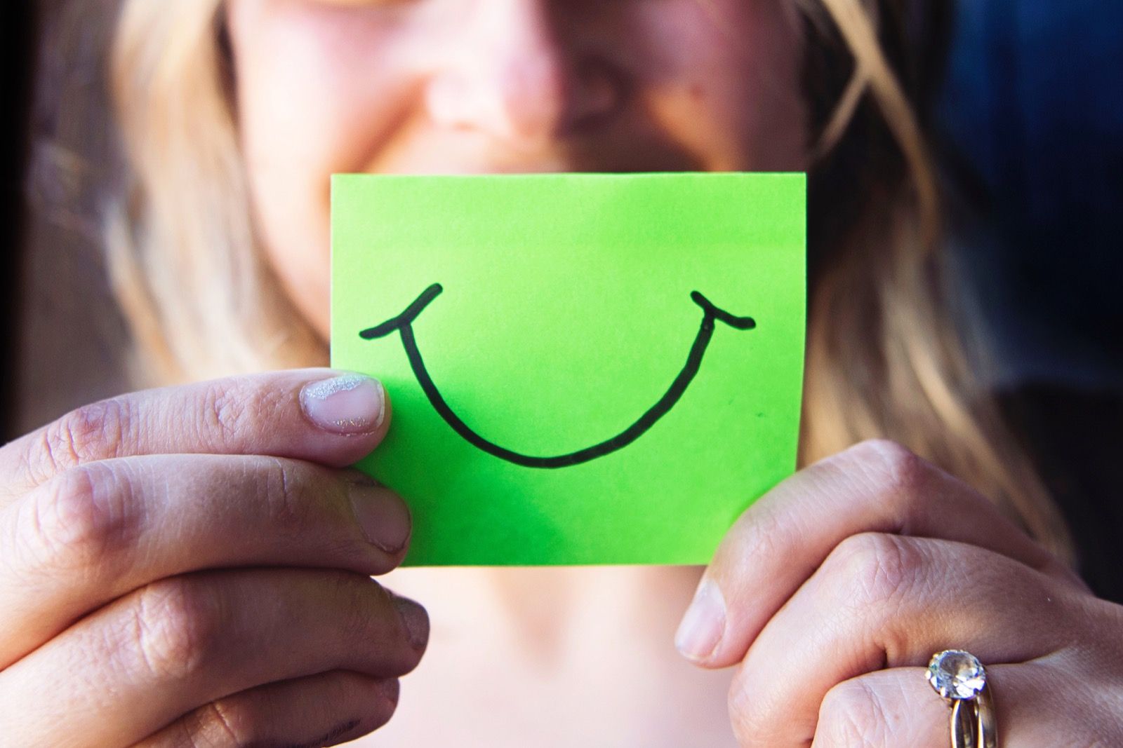 Woman holding a post-it note with a smile drawn on it