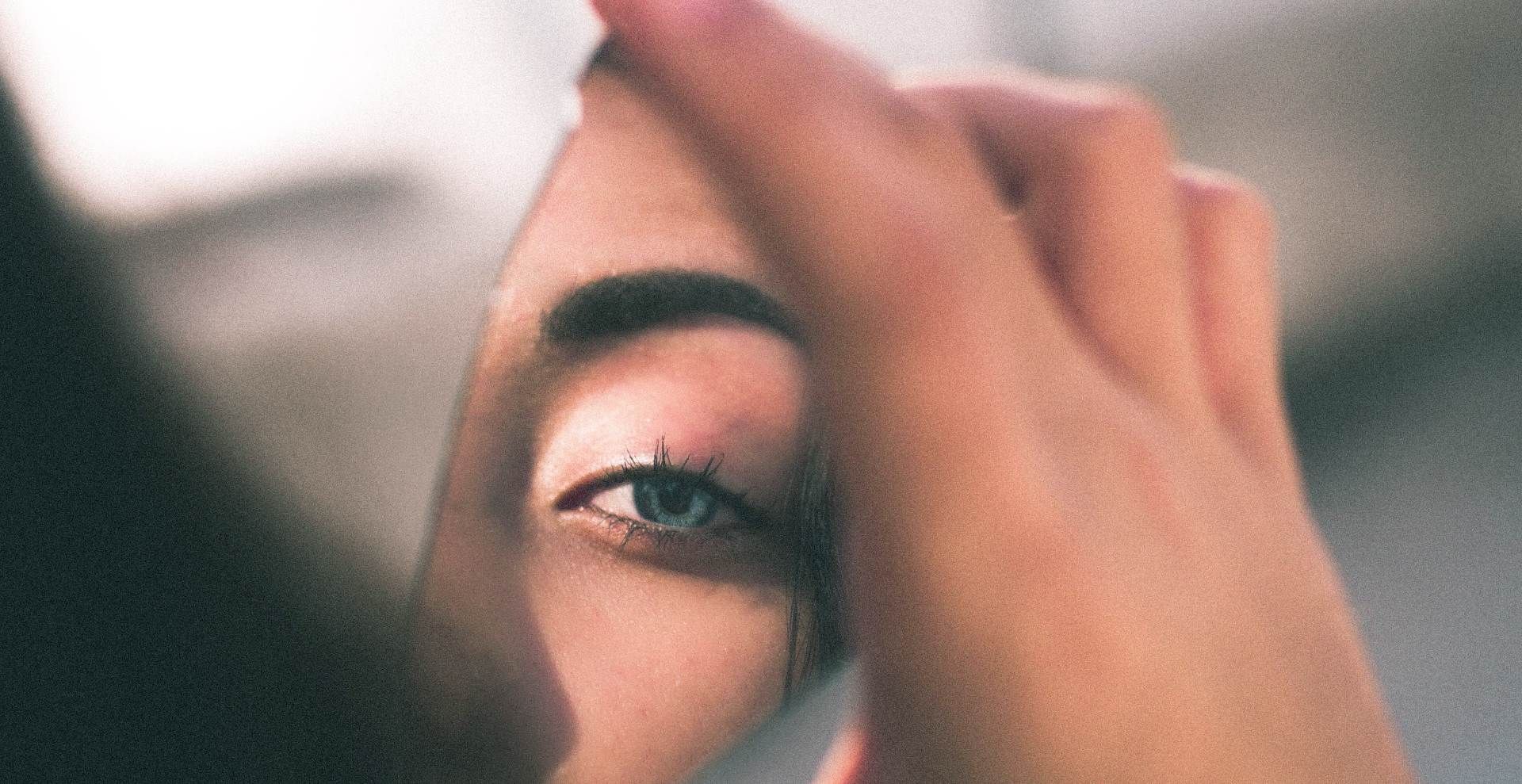 Woman looking at part of her face in the shard of a mirror