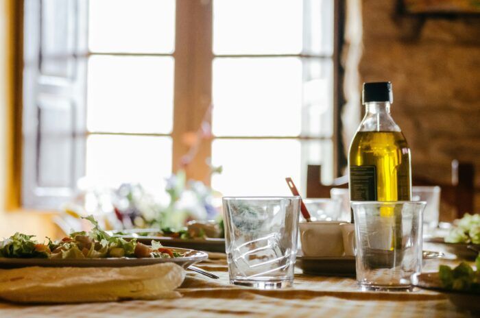 This image captures the essence of Mediterranean dining with its focus on fresh, wholesome ingredients. A bottle of olive oil stands as a centerpiece, symbolizing its vital role in this heart-healthy diet. Plates of salad and a cozy, rustic atmosphere invite you to indulge in balanced and nourishing meals. Perfect for promoting the health benefits of Mediterranean living.