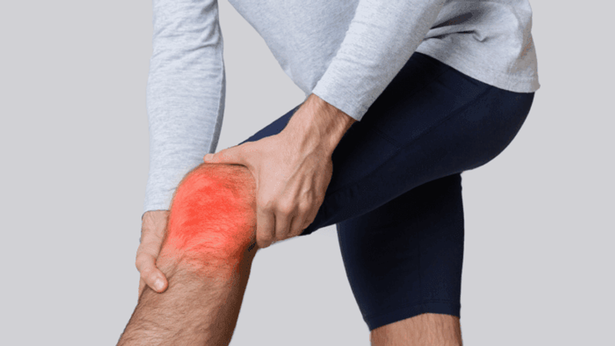 An image of a man's bent knee being grasped in pain by hands, showing joint inflammation with glowing red areas.